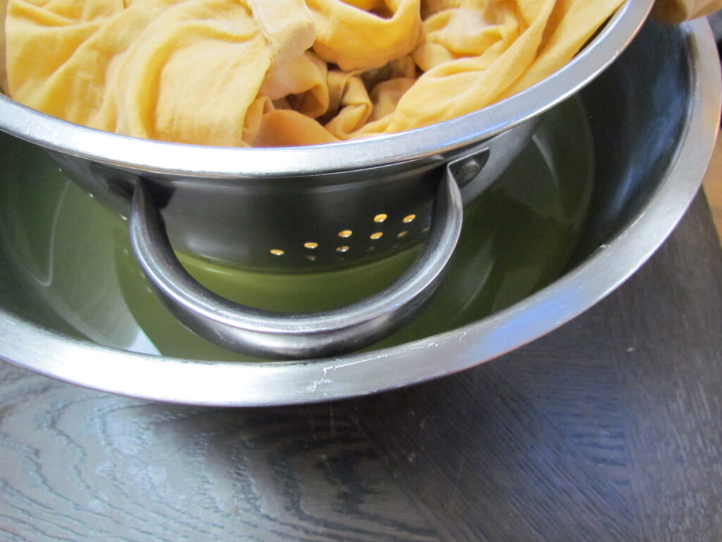 Picture of covered yogurt inside strainer after straining overnight. Whey liquid is in the bowl below.